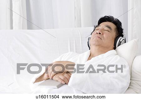 Picture - Senior man lying on sofa listening music. Fotosearch