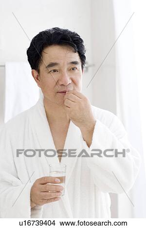 Picture - Senior man taking medicine with water in bathroom. Fotosearch
