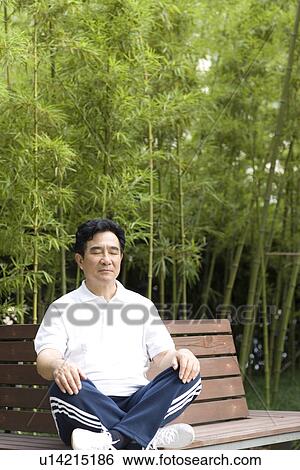 Stock Photograph - Senior man with eyes closed sitting on bench in park. Fotosearch