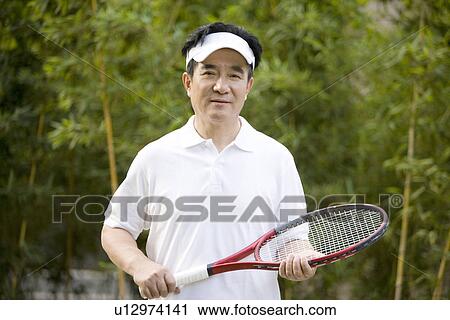 Stock Image - Senior man with tennis racket, smiling, portrait. Fotosearch