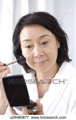 Stock Photo - Senior woman applying makeup with cosmetic brush and compact mirror. Fotosearch