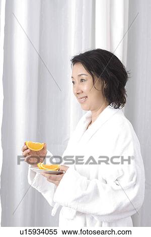 Stock Photography - Senior woman holding a sauce of orange slices. Fotosearch