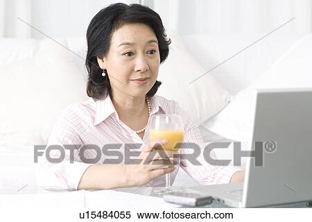 Stock Photography - Senior woman holding laptop holding a glass of juice. Fotosearch