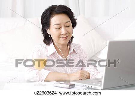 Picture - Senior woman listening music from laptop smiling in home. Fotosearch