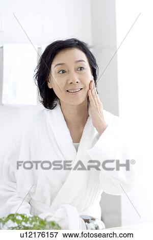Stock Photo - Senior woman looking in mirror in bathroom. Fotosearch
