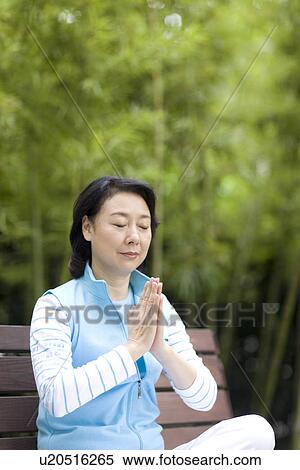 Stock Photography - Senior woman sitting on bench in prayer position outdoors. Fotosearch