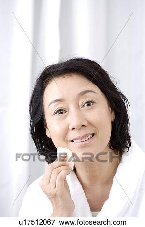 Stock Photo - Senior woman using cotton pad smiling, portrait. Fotosearch