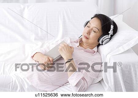 Stock Photograph - Senior woman wearing headset lying on sofa sleeping. Fotosearch