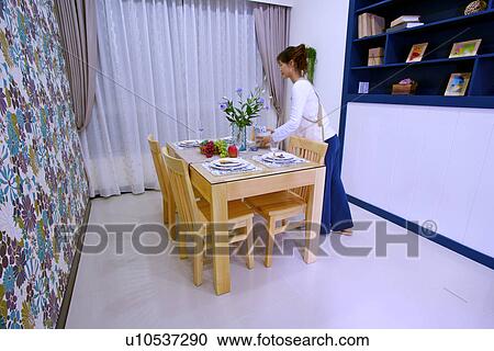 Stock Image - Young woman by dinning table. Fotosearch