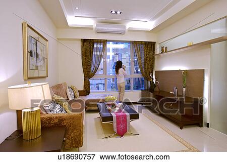 Stock Photo - Young woman by window in living room. Fotosearch