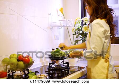 Stock Photo - Young woman cooking in kitchen. Fotosearch
