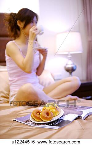 Young woman sitting on bed eating food View Large Photo Image Stock Photograph - Young woman sitting on bed eating food. Fotosearch
