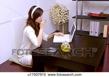 Stock Photography - Young woman sitting on mat using laptop. Fotosearch