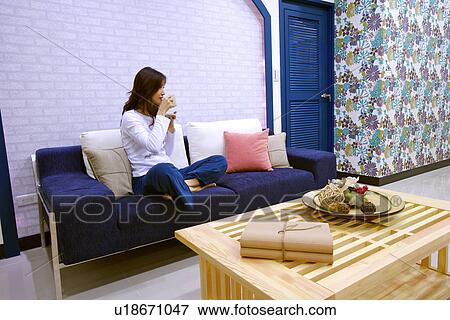 Young woman sitting on sofa drinking tea View Large Photo Image Stock Photo - Young woman sitting on sofa drinking tea. Fotosearch