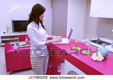 Young woman standing by counter using laptop in modern style room View Large Photo Image Stock Photo - Young woman standing by counter using laptop in modern style room. Fotosearch
