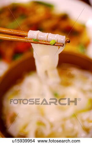 Picture - Chopsticks picking flat noodles from bowl. Fotosearch