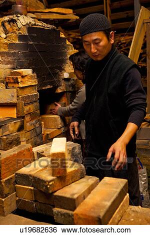Stock Photograph - Male and female potters sealing kiln's entrance, side view. Fotosearch