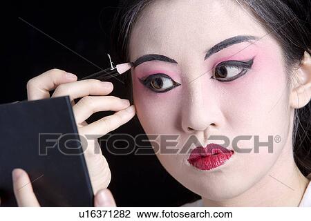 Stock Image - Beijing Opera performer applying eyebrow in mirror. Fotosearch