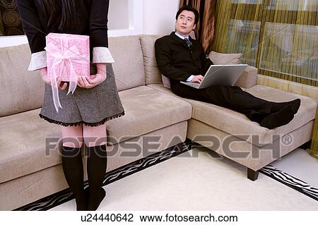Stock Image - Couple at home, wife with gifts behind back. Fotosearch