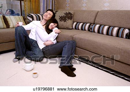 Couple embracing leaning against sofa View Large Photo Image Stock Image - Couple embracing leaning against sofa. Fotosearch