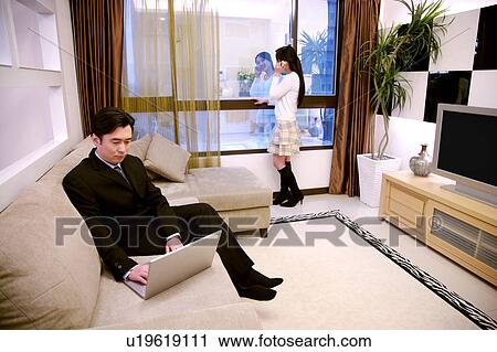 Stock Image - Couple in living room, man using laptop, woman on the phone. Fotosearch