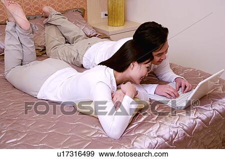 Stock Photo - Couple on bed using laptop. Fotosearch