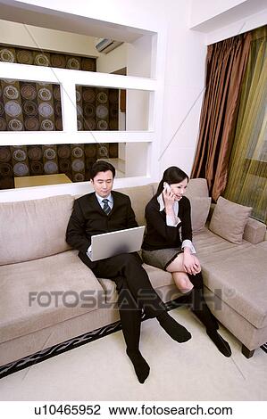 Stock Image - Couple on sofa, husband using laptop, wife on the phone. Fotosearch