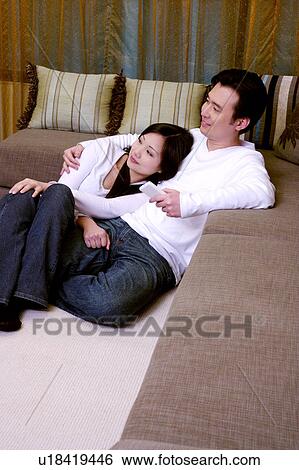 Couple sitting on floor leaning against sofa View Large Photo Image Stock Photograph - Couple sitting on floor leaning against sofa. Fotosearch