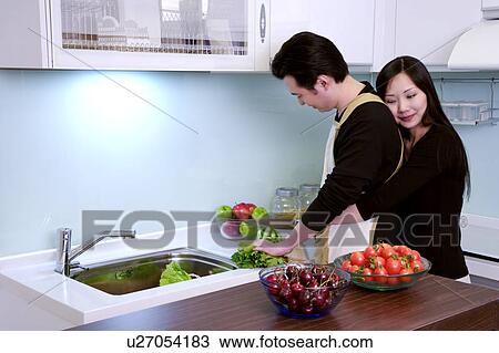 Stock Image - Man chopping vegetable, woman embracing him. Fotosearch