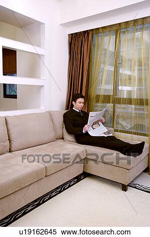 Stock Photography - Man leaning against sofa reading newspaper. Fotosearch