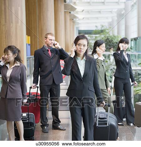 Stock Photograph - Business executives talking on mobile phones and leaving an airport lounge. Fotosearch