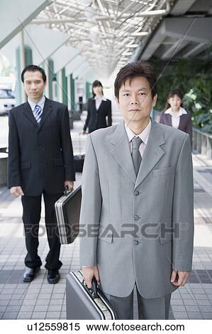 Stock Photography - Businessman standing and holding his suitcase with three business executives in the background. Fotosearch