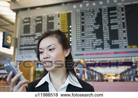 Close-up of a businesswoman at an airport holding a mobile phone View Large Photo Image Stock Photo - Close-up of a businesswoman at an airport holding a mobile phone. Fotosearch