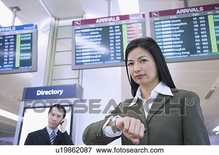 Portrait of a businesswoman with a businessman talking on a mobile phone behind her at an airport View Large Photo Image Stock Photo - Portrait of a businesswoman with a businessman talking on a mobile phone behind her at an airport. Fotosearch