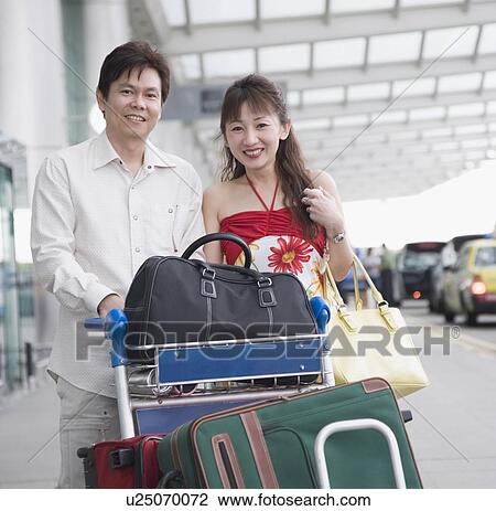 Stock Image - Portrait of a mature couple pushing a luggage cart. Fotosearch