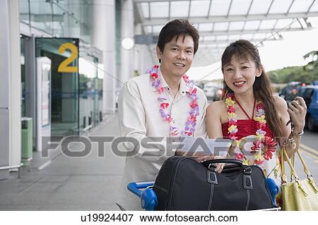 Stock Photo - Portrait of a mature couple standing with a luggage cart at an airport. Fotosearch