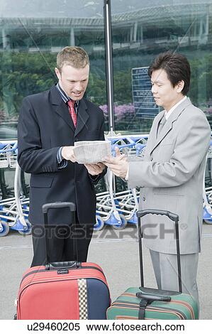 Stock Photography - Two businessmen discussing a document outside an airport. Fotosearch
