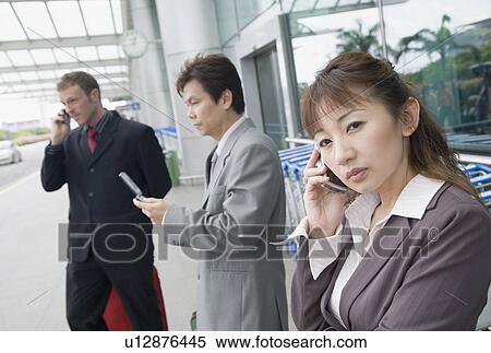 Stock Photography - Two businessmen with a businesswoman waiting at an airport lounge. Fotosearch