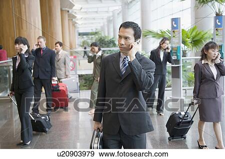 Stock Photo - Business executives talking on mobile phones and leaving an airport lounge. Fotosearch