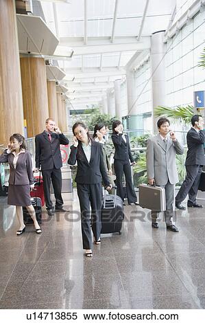 Stock Photography - Business executives talking on mobile phones and leaving an airport lounge. Fotosearch