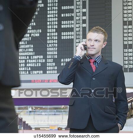Businessman standing at an airport talking on a mobile phone View Large Photo Image Stock Photo - Businessman standing at an airport talking on a mobile phone. Fotosearch