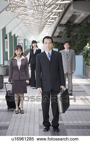 Businessman walking and holding his suitcase with three business executives in the background View Large Photo Image Stock Photography - Businessman walking and holding his suitcase with three business executives in the background. Fotosearch