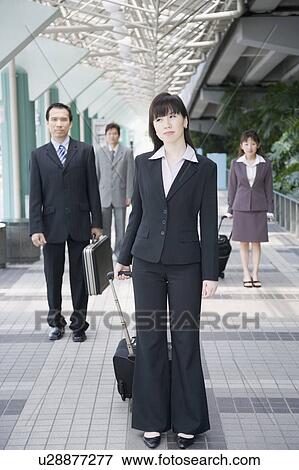 Stock Photo - Businesswoman standing and holding his luggage with three business executives in the background. Fotosearch