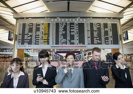 Stock Image - Five business executives standing in front of an arrival departure board at an airport. Fotosearch