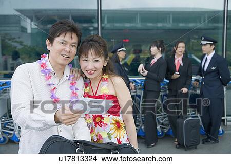 Mature couple looking at an airplane ticket with pilots and cabin crews standing in the background View Large Photo Image Picture - Mature couple looking at an airplane ticket with pilots and cabin crews standing in the background. Fotosearch