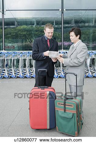 Stock Photo - Two businessmen discussing a document outside an airport. Fotosearch