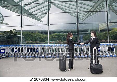 Picture - Two businesswomen shaking hands outside an airport. Fotosearch