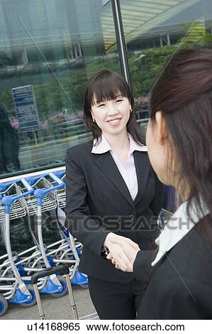 Stock Photography - Two businesswomen shaking hands outside an airport. Fotosearch
