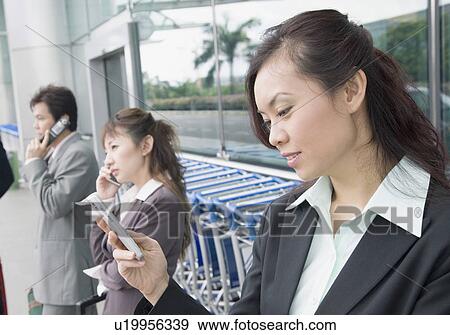 Stock Photo - Two businesswomen with a businessman waiting at an airport lounge. Fotosearch