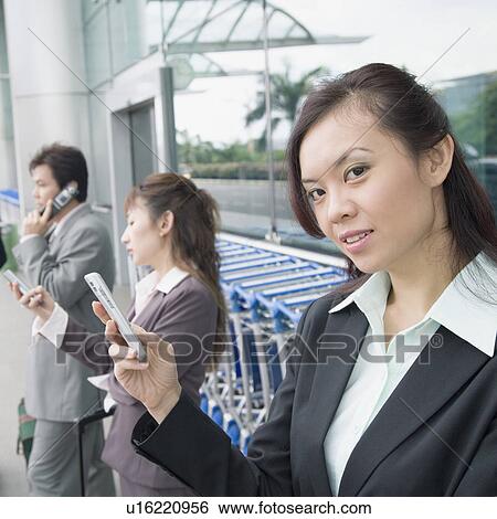 Stock Photograph - Two businesswomen with a businessman waiting at an airport lounge. Fotosearch